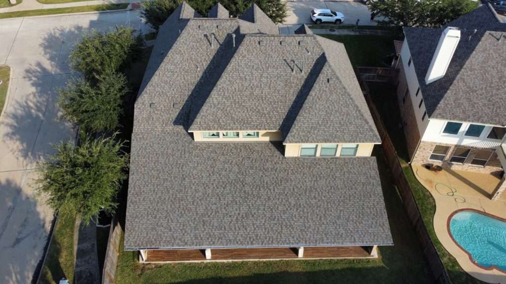 Aerial view of a residential roof featuring asphalt shingles, surrounded by trees and neighboring houses, relevant to roofing condition documentation for insurance claims.