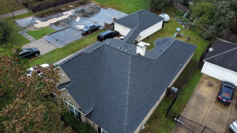 Aerial view of a residential property showcasing a recently installed asphalt shingle roof, surrounded by green lawn and parked vehicles, emphasizing Executive Roofing's quality roof replacement services in Navasota, TX.