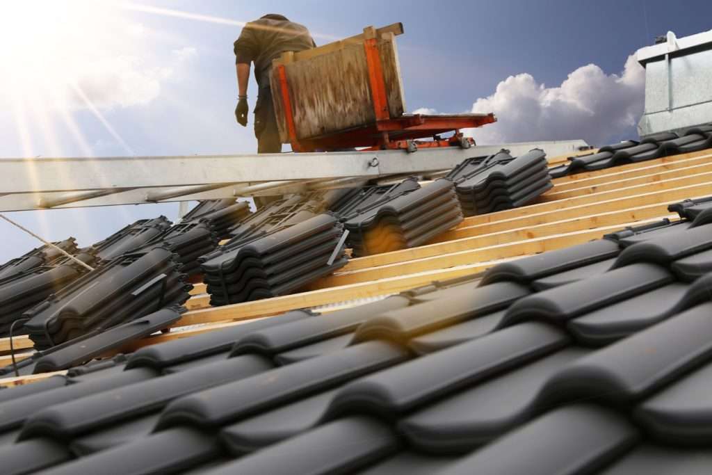 Roofing contractor installing asphalt shingles on a residential roof, showcasing roofing materials and construction process under a bright sky.