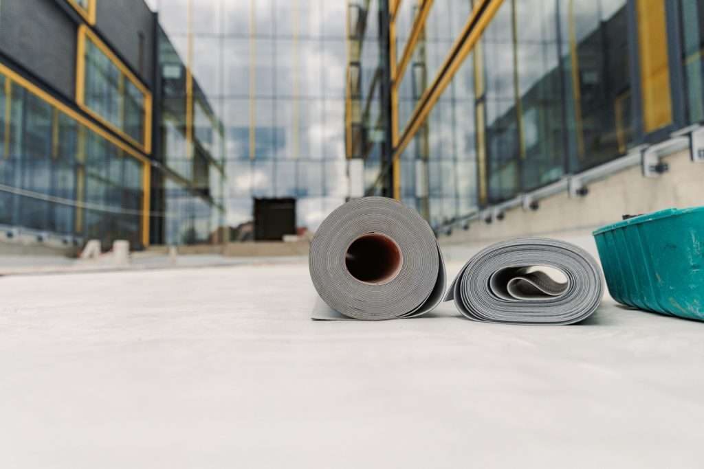 Rolls of roofing material on a commercial building site, showcasing flat roofing installation in progress, with modern glass structure in the background.