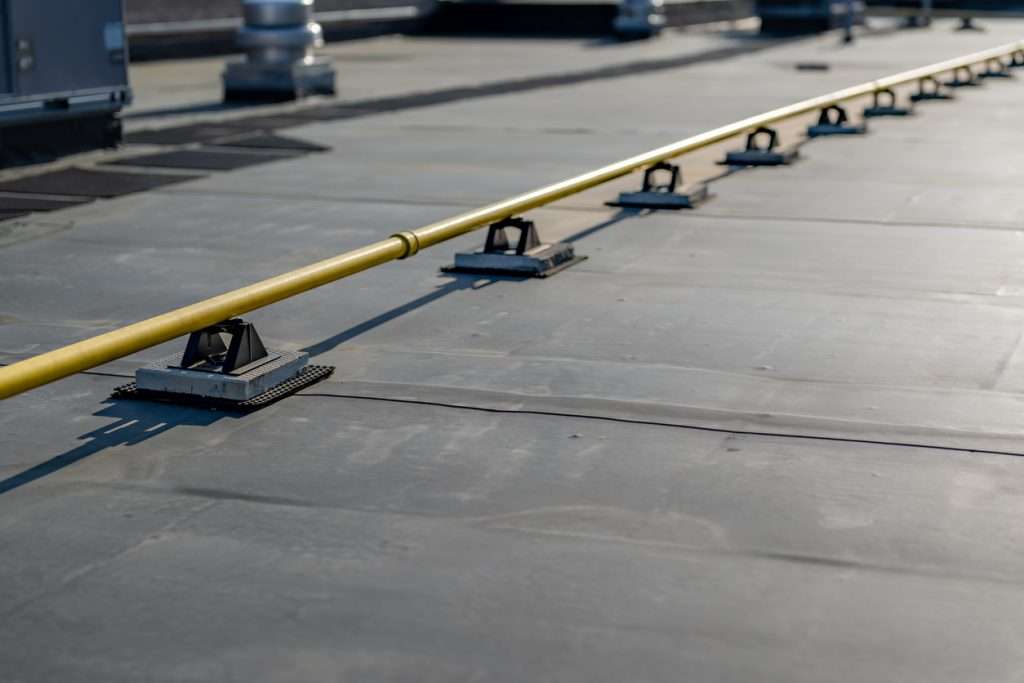 Roofing surface with yellow safety railing and support bases, illustrating features of flat roofing systems used in commercial buildings for HVAC installations and maintenance access.