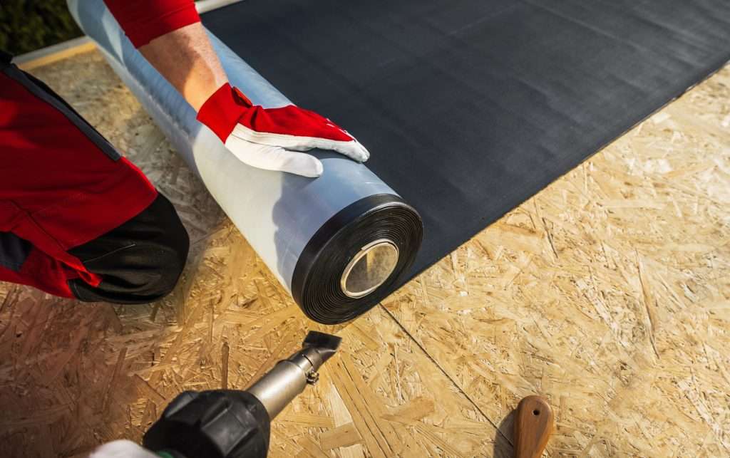Person installing a low-slope roofing membrane on a wooden surface, demonstrating commercial roofing techniques and materials.