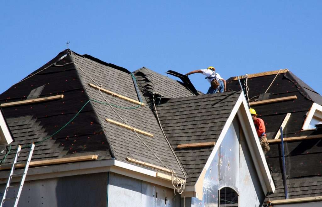 Roofers installing shingles on a steep roof, emphasizing the importance of proper ventilation for home efficiency and safety.
