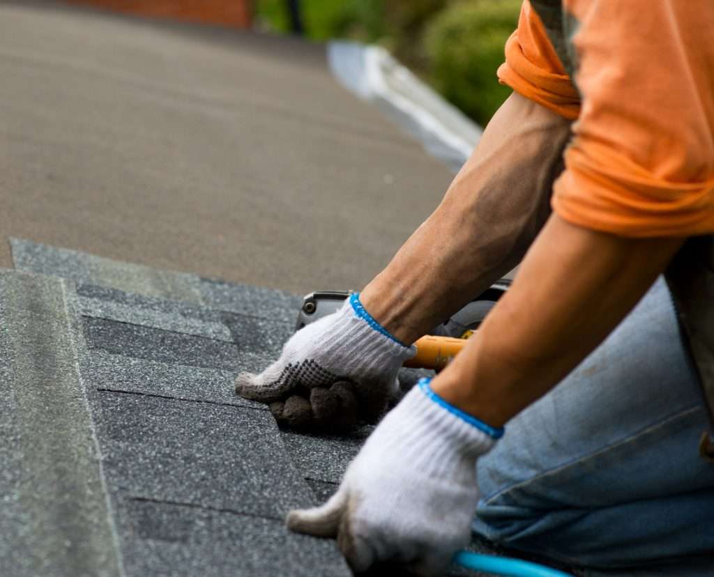 Worker installing asphalt shingles on a roof, showcasing the durability and cost-effectiveness of asphalt roofing materials.