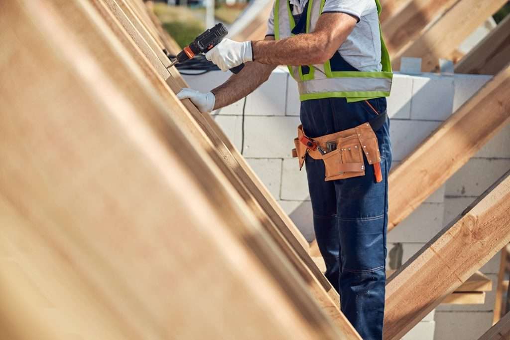 Construction worker using a power tool on a roof, surrounded by wooden framing, illustrating roofing installation relevant to insurance claims for roof replacements.