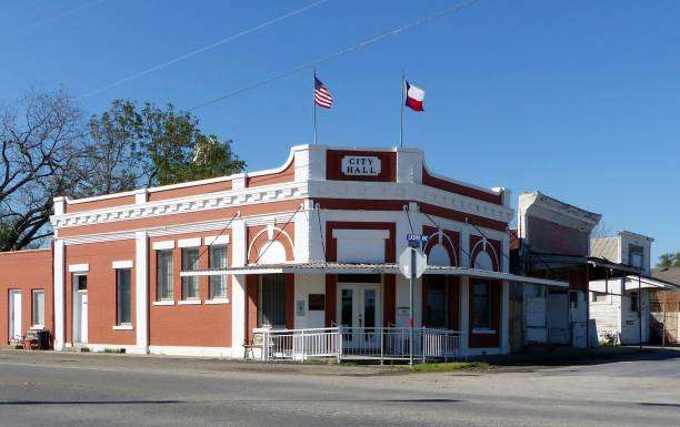 Historic City Hall building in Sealy, Texas, featuring red brick facade, American and Texas flags, and prominent architectural details.