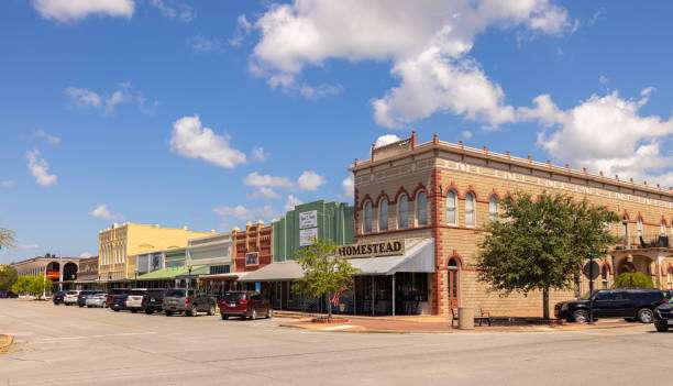 Historic downtown Sealy, Texas, featuring charming storefronts, local businesses, and parked vehicles under a blue sky with scattered clouds.