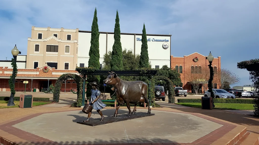 Statue of a girl with a bucket walking beside a cow in front of Blue Bell Creameries in Brenham, TX, showcasing local culture and heritage.
